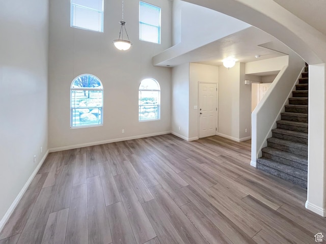 5262 W Cool Water Way, West Jordan, UT 84081 - unfurnished living room with baseboards, stairway, arched walkways, light wood-style floors, and a high ceiling