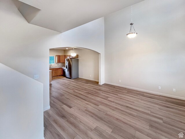 5262 W Cool Water Way, West Jordan, UT 84081 - unfurnished living room featuring arched walkways, high vaulted ceiling, baseboards, and light wood finished floors