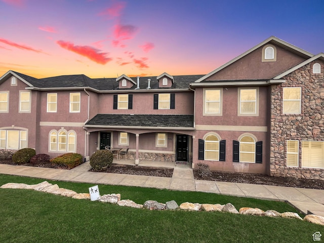 view of front of house featuring stone siding, stucco siding, and a lawn