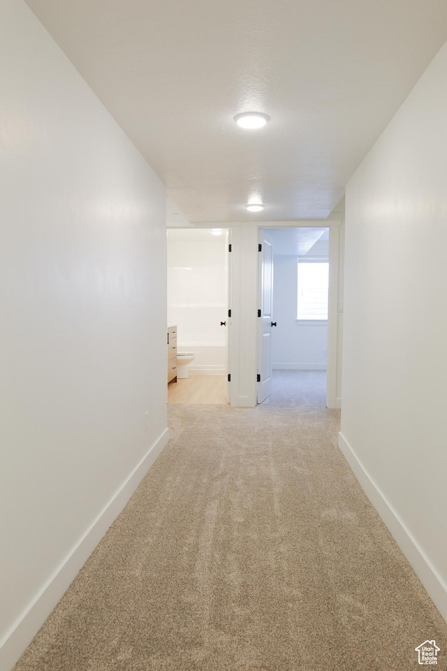 corridor with baseboards and light colored carpet