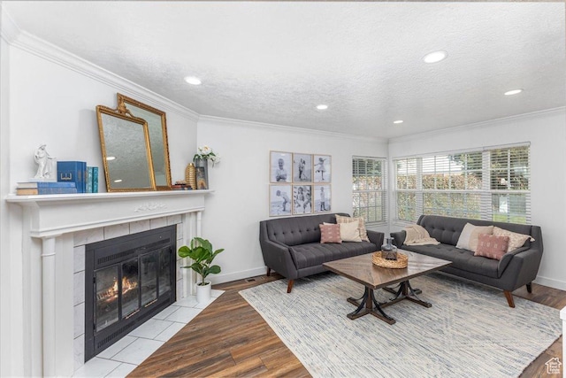living room with a tile fireplace, wood finished floors, a textured ceiling, baseboards, and ornamental molding