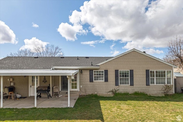 rear view of property featuring a shingled roof, a yard, and a patio area