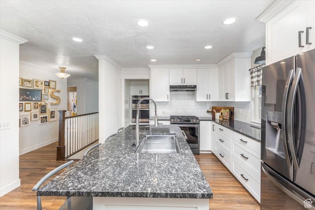 kitchen with a sink, white cabinetry, wood finished floors, under cabinet range hood, and stainless steel appliances