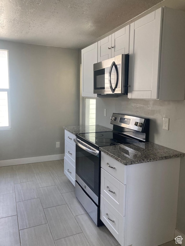 2855 Lincoln Ave, Ogden, UT 84401 - kitchen with white cabinetry, a textured ceiling, dark stone countertops, stainless steel appliances, and baseboards