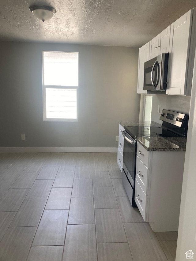 2855 Lincoln Ave, Ogden, UT 84401 - kitchen with white cabinets, a textured ceiling, baseboards, stainless steel appliances, and dark stone countertops