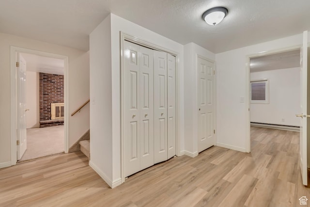 unfurnished bedroom with baseboard heating, a closet, light wood finished floors, and baseboards
