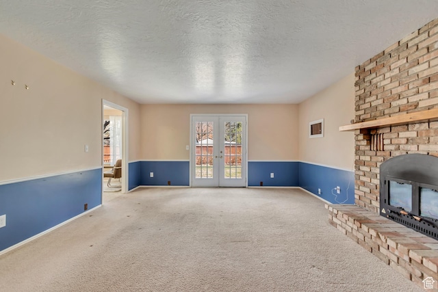 unfurnished living room with a textured ceiling, carpet floors, wainscoting, a brick fireplace, and french doors