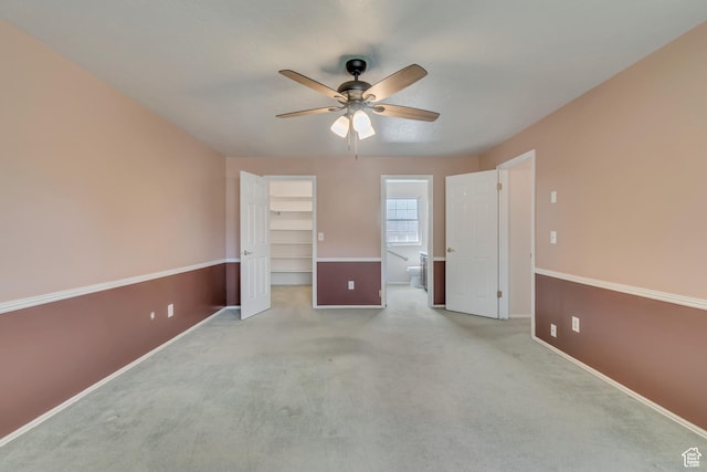 unfurnished bedroom with a closet, baseboards, ceiling fan, a walk in closet, and light colored carpet