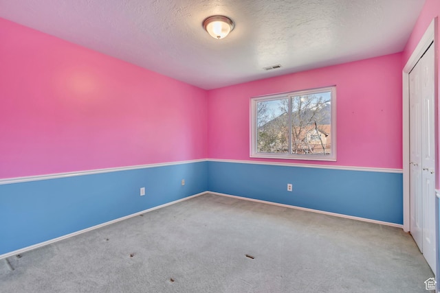 unfurnished room featuring a textured ceiling, baseboards, carpet, and visible vents