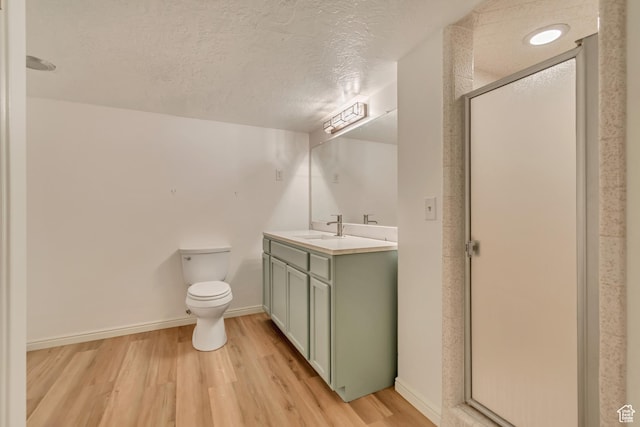 full bath with toilet, a textured ceiling, vanity, wood finished floors, and a stall shower