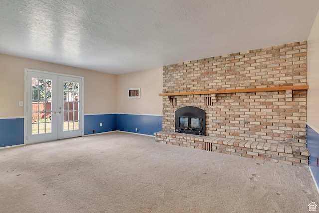 unfurnished living room featuring a fireplace, a textured ceiling, carpet flooring, wainscoting, and french doors