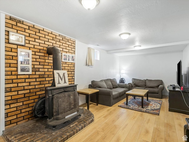 living area with a textured ceiling, wood finished floors, a wood stove, and brick wall