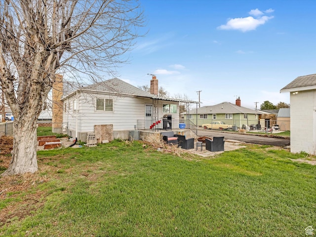 rear view of property featuring a chimney, outdoor lounge area, a patio, central AC unit, and a lawn