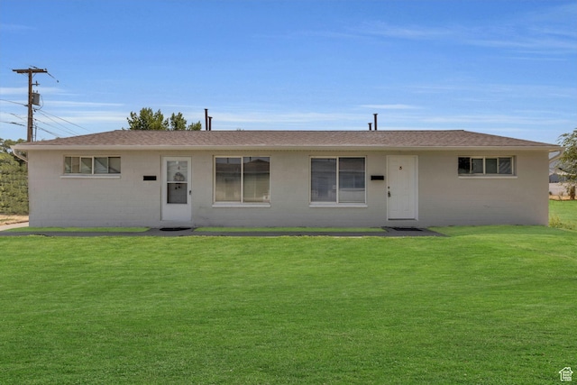 ranch-style house featuring concrete block siding, a front yard, and roof with shingles