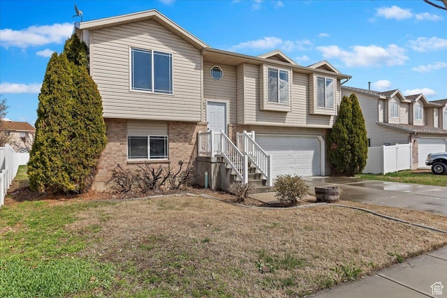 split foyer home featuring fence, an attached garage, concrete driveway, brick siding, and a front lawn