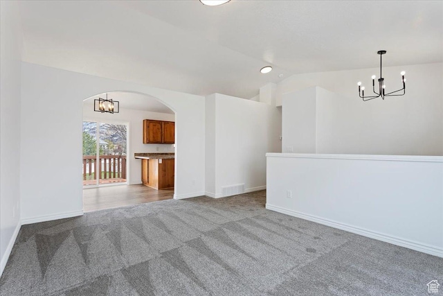 empty room with carpet, baseboards, arched walkways, vaulted ceiling, and a notable chandelier