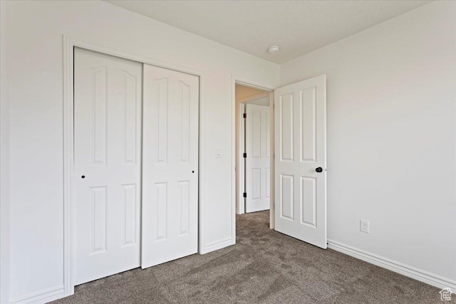 unfurnished bedroom with baseboards, a closet, and dark carpet