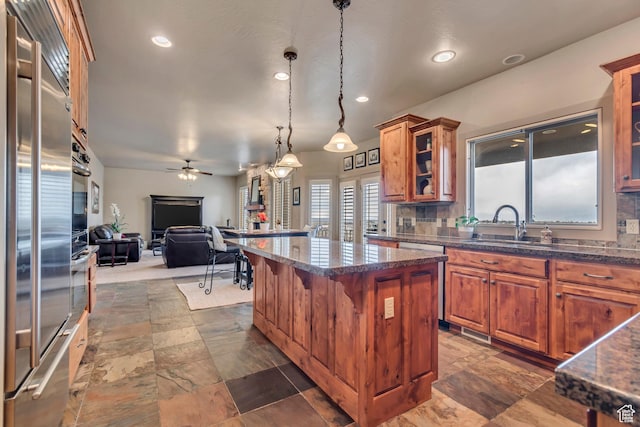 kitchen featuring a center island, open floor plan, brown cabinetry, stainless steel appliances, and ceiling fan