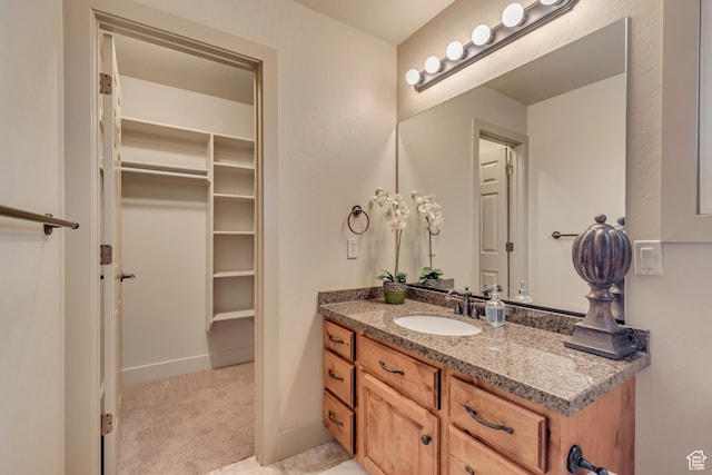 bathroom with baseboards, a walk in closet, and vanity