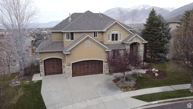 view of front facade featuring stucco siding, roof with shingles, stone siding, driveway, and a mountain view