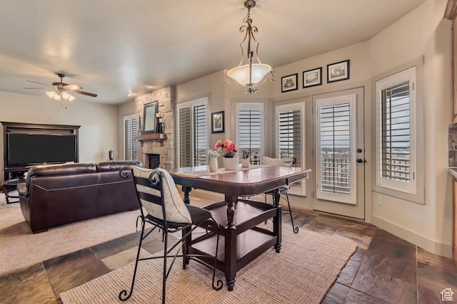dining room featuring baseboards, stone finish flooring, a ceiling fan, and a stone fireplace