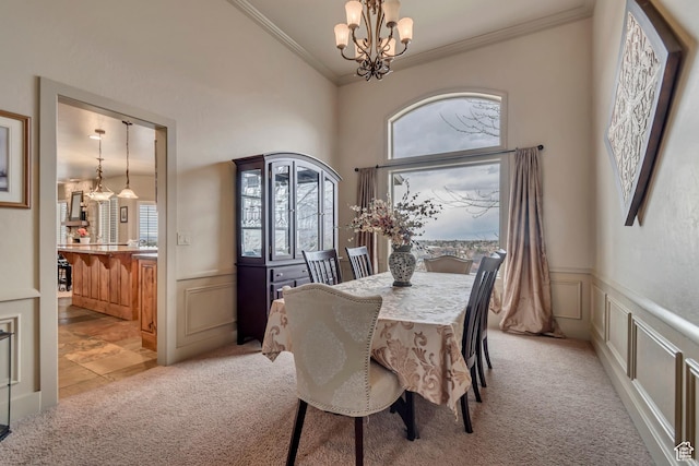 dining area with a decorative wall, crown molding, a notable chandelier, and light colored carpet