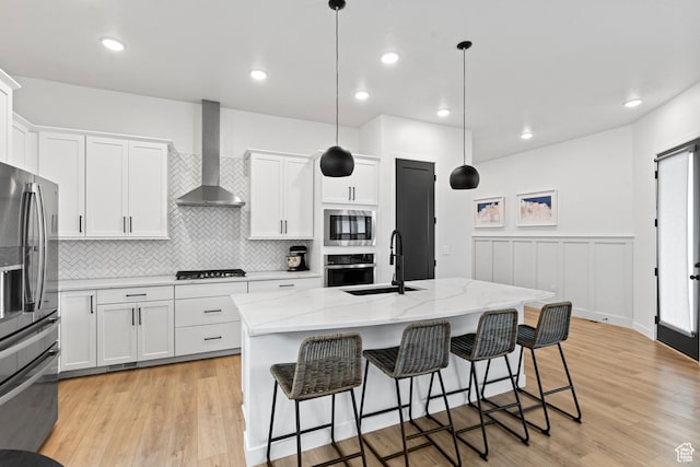 kitchen with wall chimney range hood, a sink, appliances with stainless steel finishes, and light wood-type flooring