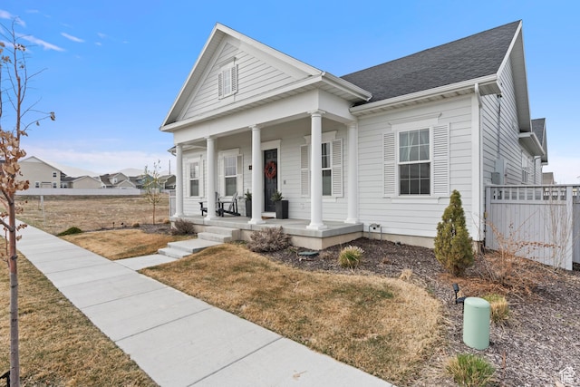 neoclassical / greek revival house featuring fence, a shingled roof, and a porch