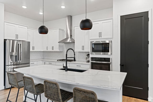 kitchen with wall chimney range hood, light wood finished floors, tasteful backsplash, and appliances with stainless steel finishes