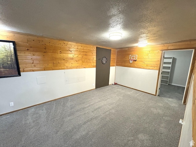 carpeted empty room with baseboards, a textured ceiling, and wood walls