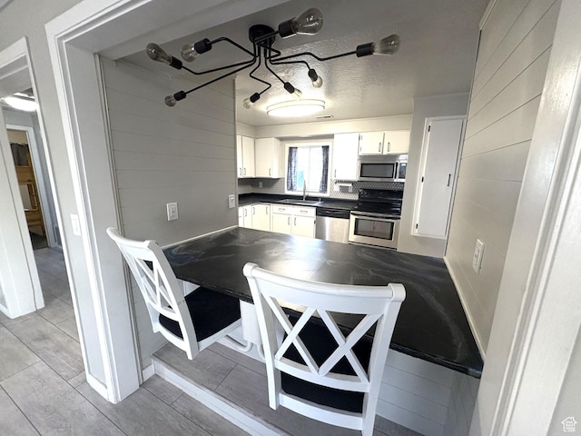 kitchen featuring a sink, light wood finished floors, stainless steel appliances, dark countertops, and white cabinets