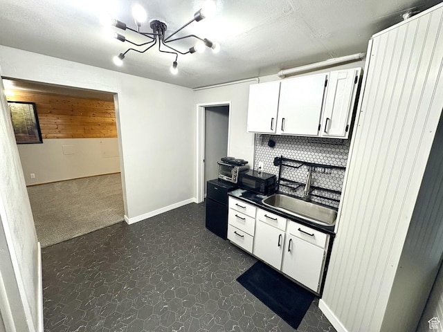kitchen featuring a sink, a chandelier, white cabinetry, baseboards, and dark countertops