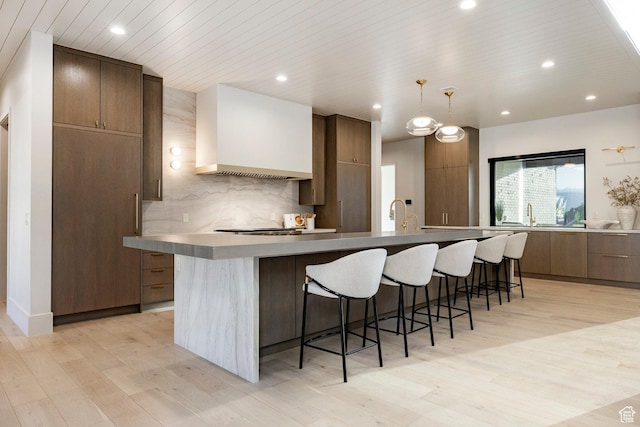 13926 S Jarvie Ln E, Draper, UT 84020 - kitchen with modern cabinets, custom range hood, a breakfast bar area, light wood-type flooring, and recessed lighting