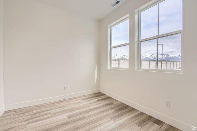 empty room with light wood-type flooring, visible vents, and baseboards