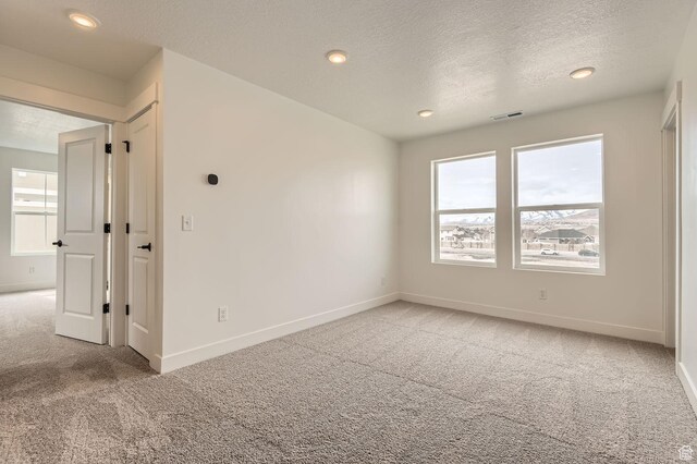 unfurnished room featuring a textured ceiling, light colored carpet, baseboards, and visible vents