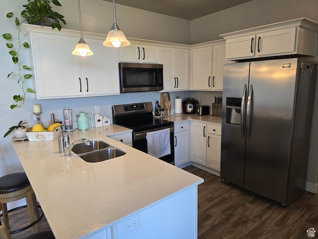 kitchen featuring dark wood-style flooring, stainless steel appliances, a sink, white cabinets, and a peninsula