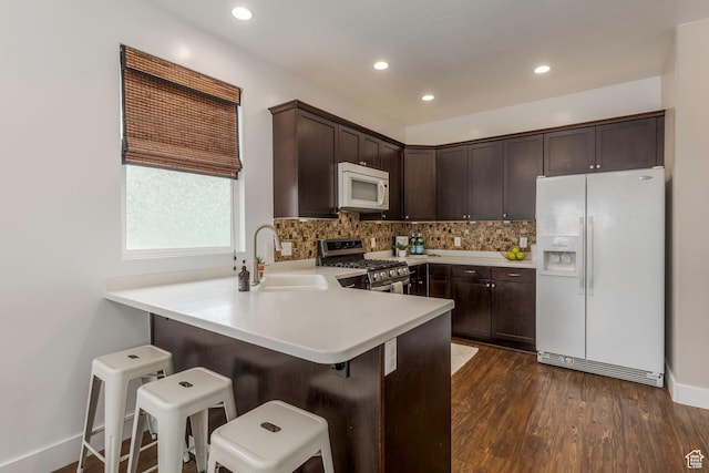 kitchen with white appliances, dark wood-style flooring, decorative backsplash, a sink, and dark brown cabinetry