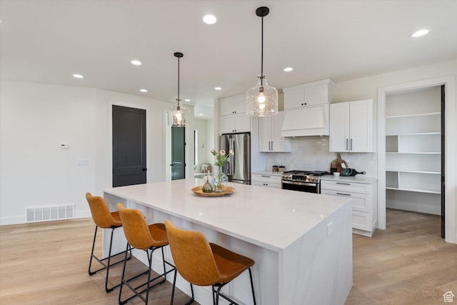 kitchen with appliances with stainless steel finishes, a center island, visible vents, custom range hood, and white cabinets
