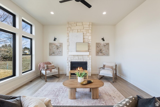 living room featuring baseboards, a fireplace, light wood-type flooring, and a ceiling fan