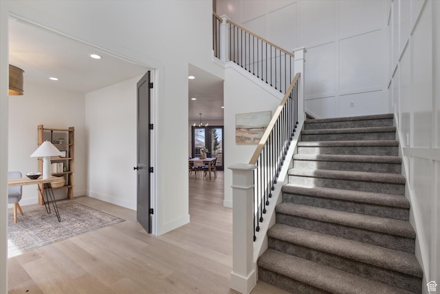 stairs featuring baseboards, a towering ceiling, wood finished floors, recessed lighting, and a notable chandelier