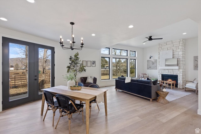 dining room featuring light wood-style flooring, a fireplace, recessed lighting, ceiling fan with notable chandelier, and french doors