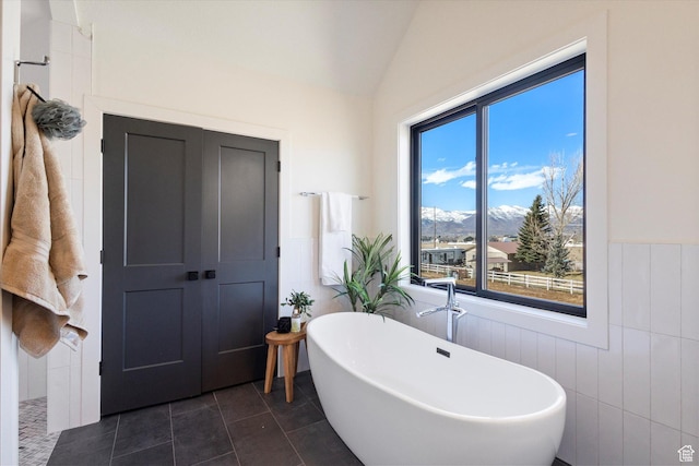 full bathroom with a soaking tub, tile patterned floors, a mountain view, vaulted ceiling, and wainscoting