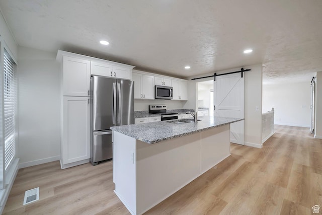 kitchen featuring white cabinetry, stainless steel appliances, a sink, an island with sink, and visible vents