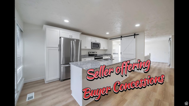 kitchen featuring visible vents, white cabinets, a barn door, a sink, and appliances with stainless steel finishes