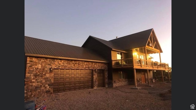 back of house with stone siding, a balcony, metal roof, an attached garage, and driveway