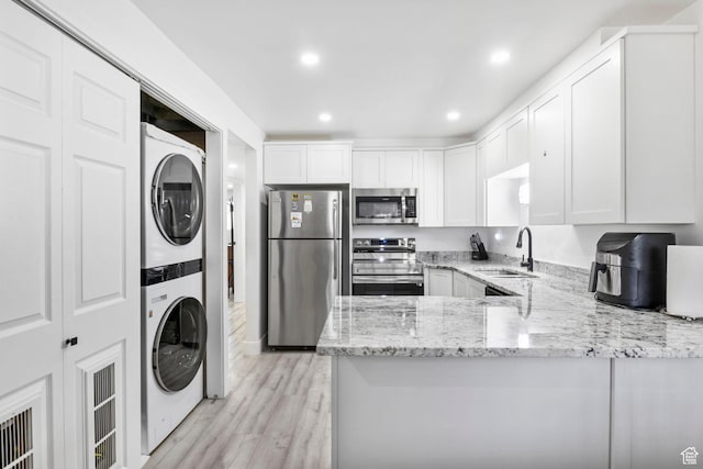 314 W Center St Unit F118, Bountiful, UT 84010 - kitchen featuring a sink, appliances with stainless steel finishes, a peninsula, stacked washer / drying machine, and light stone counters