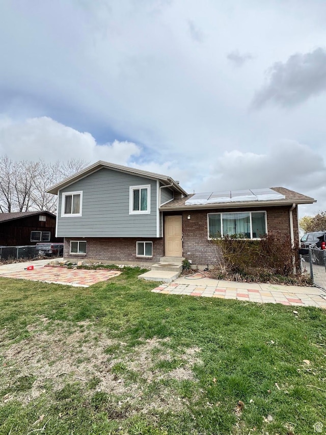view of front of property featuring fence, entry steps, solar panels, brick siding, and a front lawn