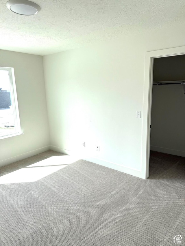 unfurnished bedroom with baseboards, carpet floors, a textured ceiling, and a spacious closet