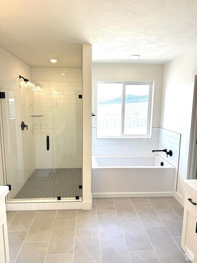 full bath with a bath, vanity, a textured ceiling, and a shower stall