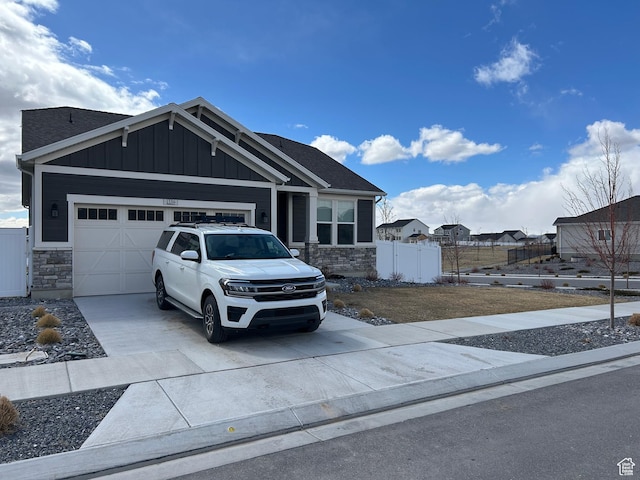 craftsman-style home with board and batten siding, fence, stone siding, an attached garage, and driveway